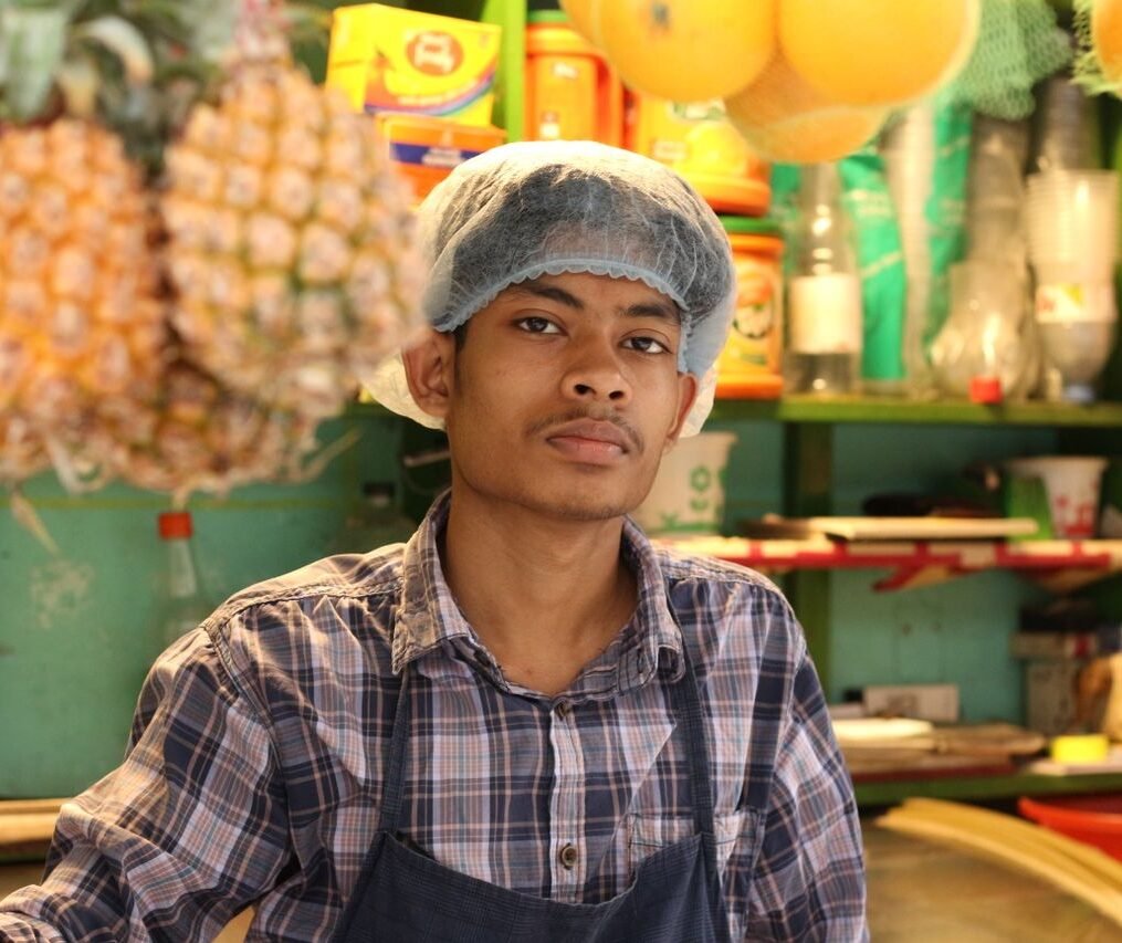 A young male vendor in a market confidently poses with tropical fruits.